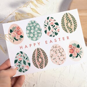 Puede incluir: Una tarjeta blanca con el texto "Happy Easter" y ocho huevos de Pascua con estampado floral. Los huevos son en tonos de rosa, verde y marr&oacute;n.
