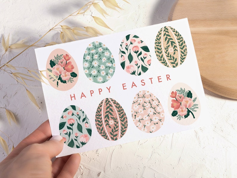 Puede incluir: Una tarjeta blanca con el texto "Happy Easter" y ocho huevos de Pascua con estampado floral. Los huevos son en tonos de rosa, verde y marr&oacute;n.