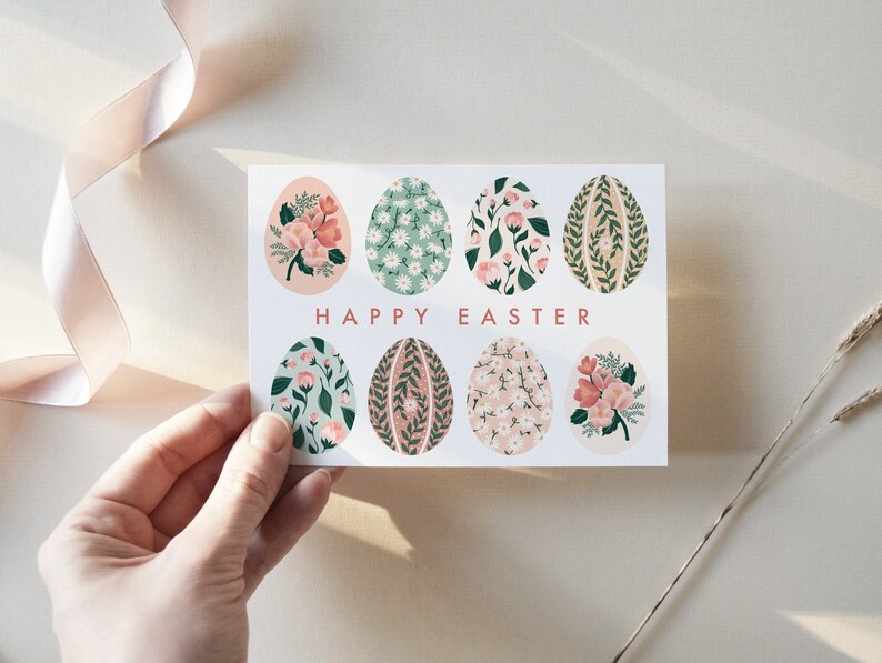 Puede incluir: Una tarjeta blanca con el texto "Happy Easter" en letras rosas. La tarjeta est&aacute; decorada con ocho huevos de color pastel, cada uno con un patr&oacute;n floral diferente.