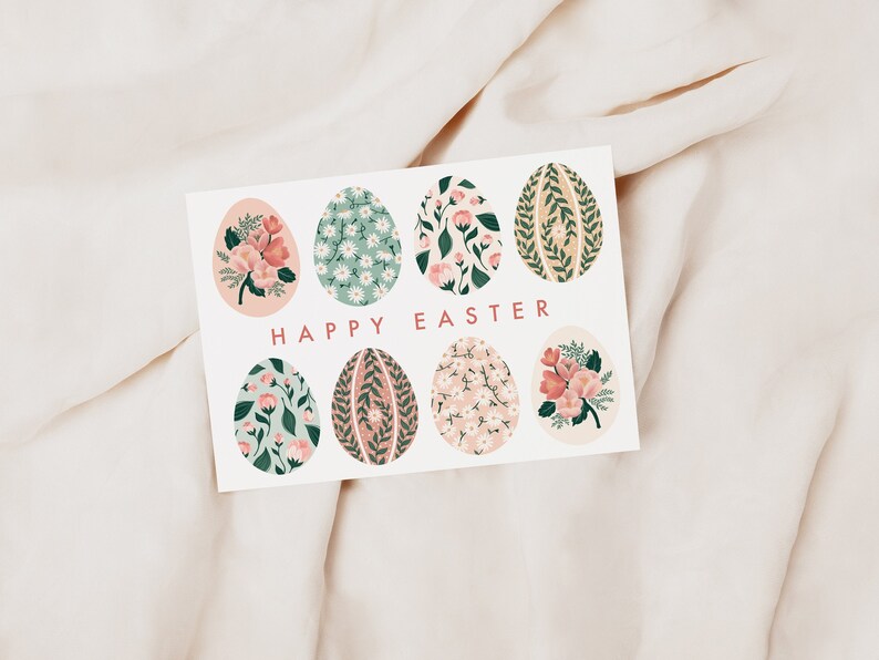 Puede incluir: Una tarjeta blanca con un dise&ntilde;o floral. La tarjeta presenta ocho huevos de Pascua de color rosa pastel y verde con patrones florales. El texto "Feliz Pascua" est&aacute; impreso en rosa en la tarjeta.