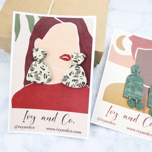 K&ouml;nnte beinhalten: Zwei Karten mit Illustrationen von Personen, die auff&auml;llige Ohrringe tragen. Die Ohrringe sind aus Polymer Clay gefertigt und haben einen Leopardenmuster und ein gr&uuml;nes Blattdesign. Die Karten zeigen den Text "Ivy and Co." und den Social-Media-Handle "@ivyandco".