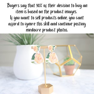 Puede incluir: Un par de pendientes colgantes florales blancos con flores amarillas y hojas verdes. Los pendientes se muestran en un soporte dorado.