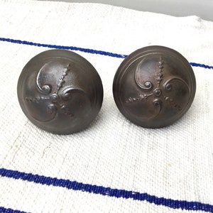 May include: Two antique, dark brown, metal door knobs with intricate floral designs.