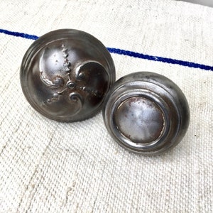 May include: Two antique metal door knobs. One knob has a decorative design with a swirl pattern. The other knob is plain.