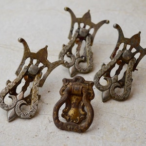 May include: Five antique drawer pulls, three are ornate and silver in color, and two are a more simple design in a brass color.