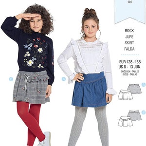Puede incluir: Patrón de costura Burda Kids con dos conjuntos infantiles. Una niña lleva un jersey azul marino con bordado floral y una falda a cuadros. La otra lleva una blusa blanca y una falda vaquera. El número de patrón es 9336.