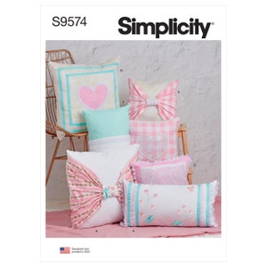 May include: A sewing pattern for making seven different decorative cushions. The cushions are in various shades of pink, white, and blue with different embellishments, including bows, hearts, and lace. The pattern is called "Simplicity" and the number is "S9574".