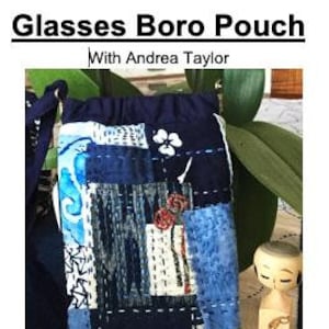 May include: A blue and white patchwork fabric pouch with a drawstring closure. The pouch is decorated with a white flower and red stitching. The pouch is designed to hold glasses.