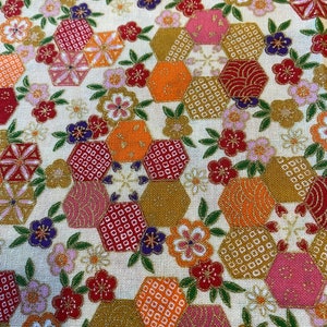 May include: Close-up of a fabric with a cream background. The fabric has a repeating pattern of hexagonal shapes in gold, orange, red, and pink, with floral and geometric designs. Small purple flowers and green leaves are also present.