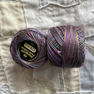 May include: Two spools of embroidery floss in shades of brown, purple, and blue. The spools are labelled "Wonderfil Petite Cotton Egyptian  #8  EZM1071 5g Double Gassed"