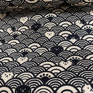 Peut inclure: Gros plan sur un tissu avec un motif répétitif de chats noirs et de motifs en forme de vagues sur un fond crème. Les chats ont des visages simples et stylisés. Le tissu est adapté à la couture ou aux projets d'artisanat.