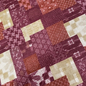 May include: A fabric featuring a patchwork design of rectangular and square blocks in shades of deep burgundy, rust orange, and cream. The pattern includes various geometric motifs, including interlocking circles, dots, and lines.