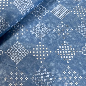 May include: Close-up of blue fabric featuring a repeating pattern of white geometric shapes. The design includes squares, diamonds, and starbursts, creating a textured appearance. The fabric has a slightly faded, vintage look.