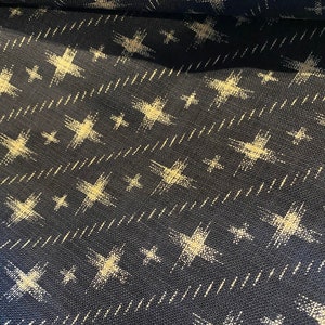 Puede incluir: Tela azul marino con un patrón de estrellas blancas. Las estrellas son estilizadas y tienen un aspecto ligeramente desgastado.