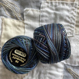 Könnte beinhalten: Zwei Spulen Wonderfil Petite Cotton Garn in Blautönen, Grün und Braun. Die Spulen sind mit "Wonderfil Petite Cotton #8", "EZM1098" und "50g" beschriftet.