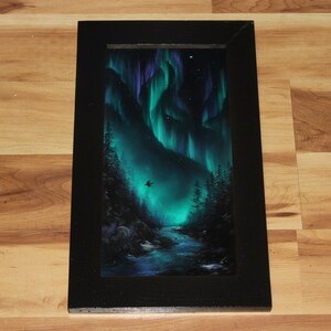 May include: A framed painting of a dark green forest with a river flowing through it. The sky is a deep blue with green and purple aurora borealis lights. A small black bird flies in the sky.