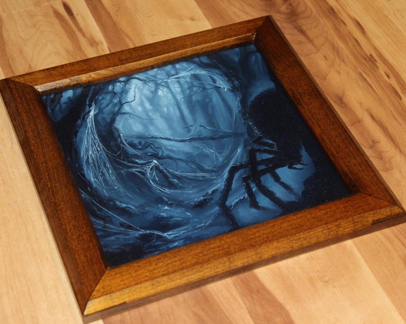 May include: A square wooden frame containing a dark blue and black painting of a forest scene. The artwork depicts a dense, shadowy woodland area with intricate, light-colored spiderwebs stretching across the trees and a large spider silhouette.