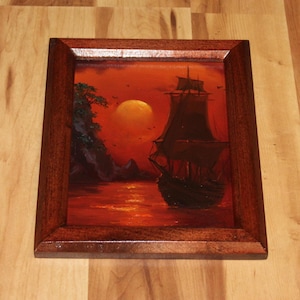 Pu&ograve; includere: Un dipinto a olio incorniciato raffigurante un veliero scuro su un mare rosso vibrante al tramonto. Un grande sole giallo brillante &egrave; sospeso nel cielo vicino a una scogliera rocciosa con fogliame verde. L'opera &egrave; racchiusa in una cornice in legno.