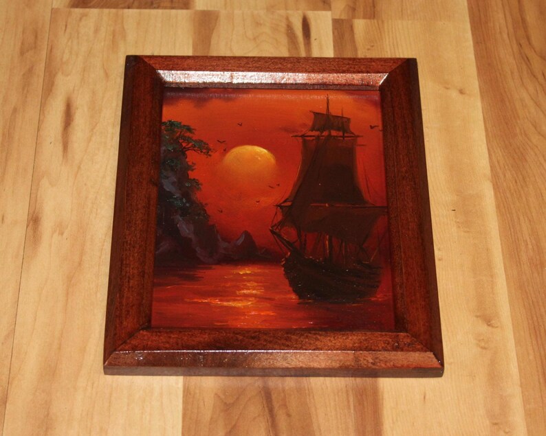 Pu&ograve; includere: Un dipinto a olio incorniciato raffigurante un veliero scuro su un mare rosso vibrante al tramonto. Un grande sole giallo brillante &egrave; sospeso nel cielo vicino a una scogliera rocciosa con fogliame verde. L'opera &egrave; racchiusa in una cornice in legno.