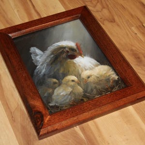 May include: A framed painting of a hen with three chicks. The hen is white with a red comb, and the chicks are yellow. The painting is in a dark brown wooden frame, and the background is dark.