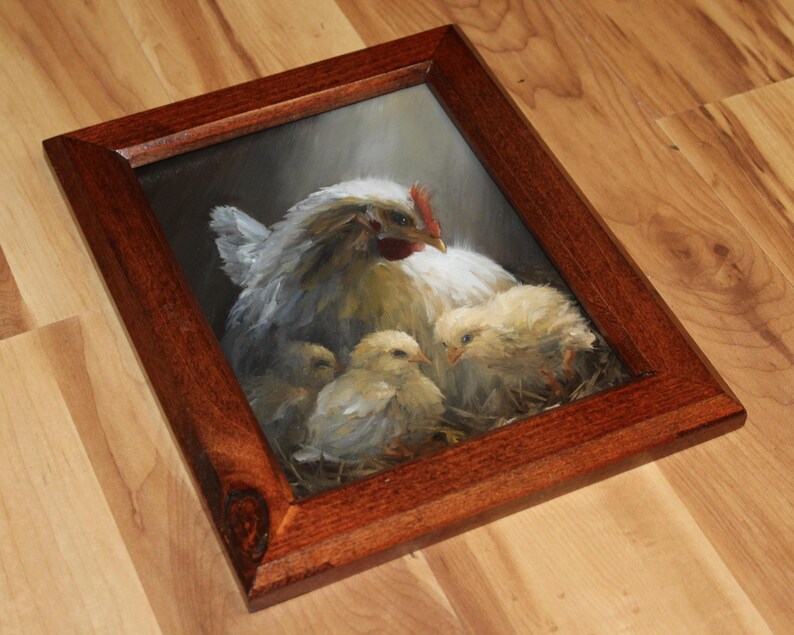 May include: A framed painting of a hen with three chicks. The hen is white with a red comb, and the chicks are yellow. The painting is in a dark brown wooden frame, and the background is dark.