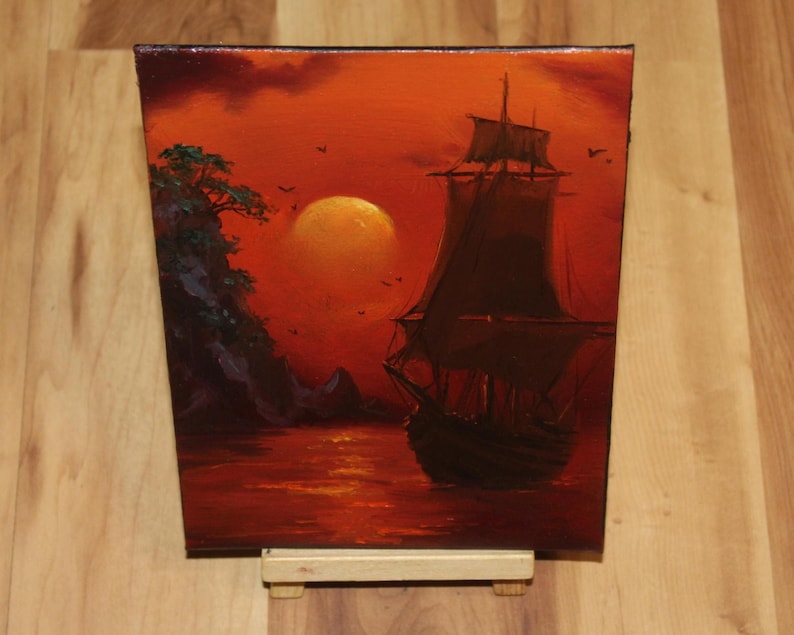 Pu&ograve; includere: Un dipinto a olio su tela che raffigura la sagoma scura di un veliero sull'acqua durante un vibrante tramonto arancione. Un grande sole luminoso &egrave; sospeso nel cielo vicino a una scogliera rocciosa con alberi di colore verde scuro.