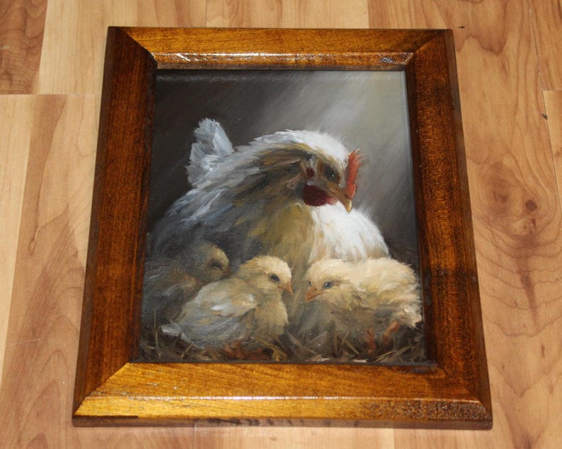 May include: Oil painting of a hen with three chicks, framed in a dark wood. The hen is white with gray shading, a red comb, and a yellow beak. The chicks are fluffy yellow. The background is dark, with light shining on the hen and chicks.