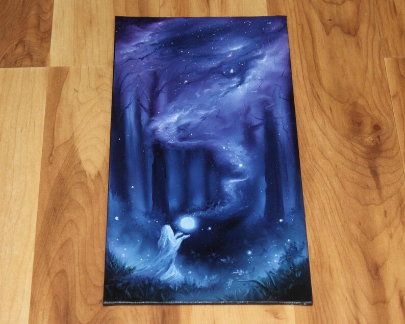 May include: A rectangular canvas painting featuring a dark forest scene in shades of blue and purple. A figure stands in the foreground holding a glowing white orb, from which a swirling mist rises into the starry night sky above the trees.