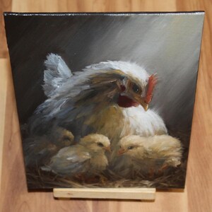 May include: An oil painting depicts a white hen with a red comb and three yellow chicks nestled in a nest. The hen is the focal point, with soft, feathery details. The background is a dark, shaded area with a spotlight effect.