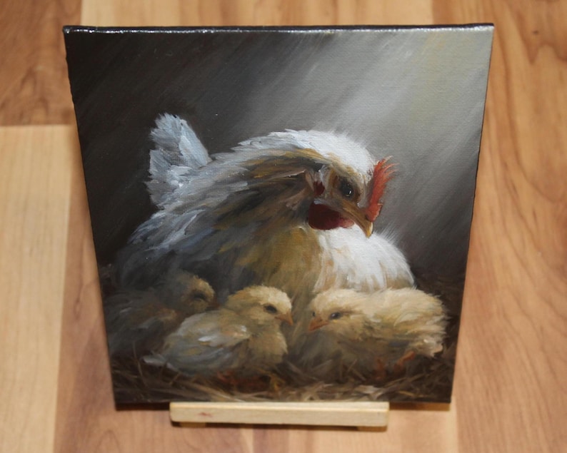May include: An oil painting depicts a white hen with a red comb and three yellow chicks nestled in a nest. The hen is the focal point, with soft, feathery details. The background is a dark, shaded area with a spotlight effect.