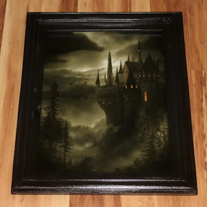 May include: A framed print of a gothic castle on a cliff, set against a dark, stormy sky. The artwork features a detailed depiction of the castle with illuminated windows, surrounded by trees and a misty landscape. The frame is black.