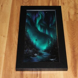 May include: A framed painting of a dark green forest with a river flowing through it. The sky is a vibrant green and purple, with a dark silhouette of a bird flying in the sky. The painting is framed in a black frame.