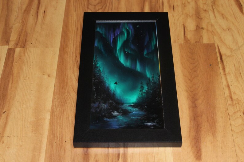 May include: A framed painting of a dark green forest with a river flowing through it. The sky is a vibrant green and purple, with a dark silhouette of a bird flying in the sky. The painting is framed in a black frame.