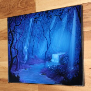 May include: A framed painting depicts a mystical forest scene. The artwork features a waterfall, a flowing river, and a spectral figure, all bathed in shades of blue and purple. The trees and foliage create a sense of depth and tranquility.