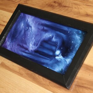 May include: A rectangular black frame containing a vibrant digital print of a dark, ethereal forest scene. The artwork features deep blue and purple hues, a glowing orb held by a figure, and a set of stairs leading into a misty, mysterious background.