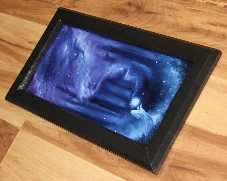 May include: A rectangular black frame containing a vibrant digital print of a dark, ethereal forest scene. The artwork features deep blue and purple hues, a glowing orb held by a figure, and a set of stairs leading into a misty, mysterious background.