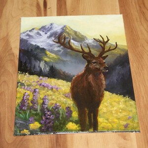May include: An oil painting depicting a deer with large antlers in a field of yellow and purple wildflowers. The background shows a mountain range with snow-covered peaks and a soft, yellow sky. The deer is brown with a dark brown nose.