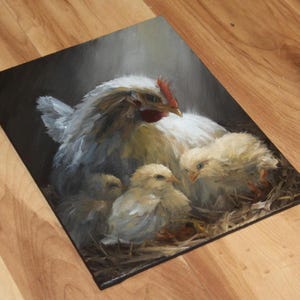 May include: An oil painting depicts a white hen with a red comb, sheltering three yellow chicks in a nest of straw. The hen's feathers are detailed with shades of gray and white, creating a soft, realistic texture. The artwork is set against a dark background.