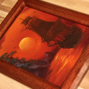 Pu&ograve; includere: Un dipinto quadrato in una cornice di legno marrone scuro che raffigura un veliero sull'acqua al tramonto. La scena presenta un grande sole arancione, sagome scure di una nave e alberi, e vivaci tonalit&agrave; di rosso e arancione nel cielo.