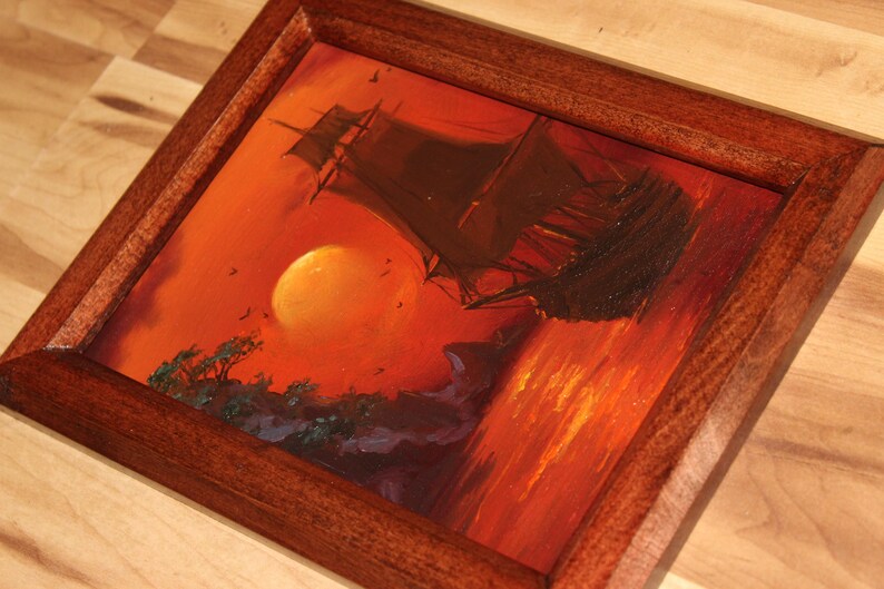 Pu&ograve; includere: Un dipinto quadrato in una cornice di legno marrone scuro che raffigura un veliero sull'acqua al tramonto. La scena presenta un grande sole arancione, sagome scure di una nave e alberi, e vivaci tonalit&agrave; di rosso e arancione nel cielo.