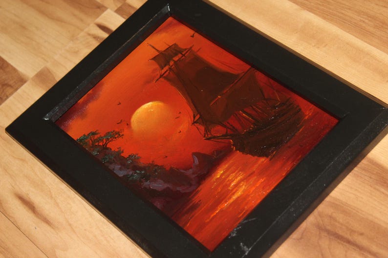 Pu&ograve; includere: Un dipinto incorniciato che raffigura un veliero sull'acqua durante un tramonto. La scena presenta un grande sole arancione, sagome scure di una nave e di una costa rocciosa, e vivaci tonalit&agrave; di rosso e arancione sull'acqua.