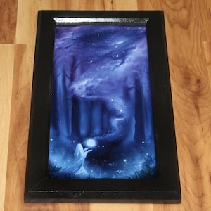May include: A rectangular framed painting featuring a dark forest scene in shades of blue and purple. A figure stands in the foreground holding a glowing white orb, while a swirling mist rises toward a starry sky above the silhouetted trees.