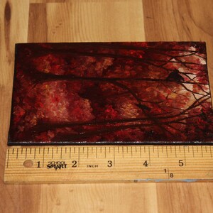 K&ouml;nnte beinhalten: Ein kleines rechteckiges Gem&auml;lde, das eine Waldszene mit rotem und braunem Laub und dunklen &Auml;sten darstellt. Das Gem&auml;lde ist etwa 15 cm lang und befindet sich auf einer Holzoberfl&auml;che.