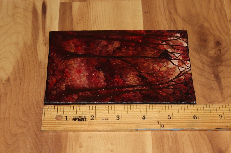 K&ouml;nnte beinhalten: Ein kleines rechteckiges Gem&auml;lde, das eine Waldszene mit rotem und braunem Laub und dunklen &Auml;sten darstellt. Das Gem&auml;lde ist etwa 15 cm lang und befindet sich auf einer Holzoberfl&auml;che.