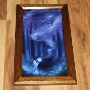 May include: A rectangular framed print featuring a dark blue forest scene at night. A figure in a white robe stands in the foreground holding a glowing orb. Swirling blue mist rises from the orb into the trees under a starry night sky.