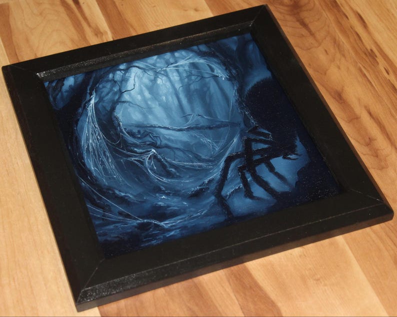 May include: A square wall art piece featuring a dark, moody illustration of a spider in a web-filled forest. The artwork is rendered in shades of deep blue and black, encased in a simple black frame, depicting a forest scene with a large spider.