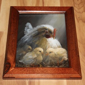 May include: A framed painting depicts a hen with three chicks. The hen is white with gray shading, a red comb, and a yellow beak. The chicks are yellow and fluffy. The frame is a dark brown wood.