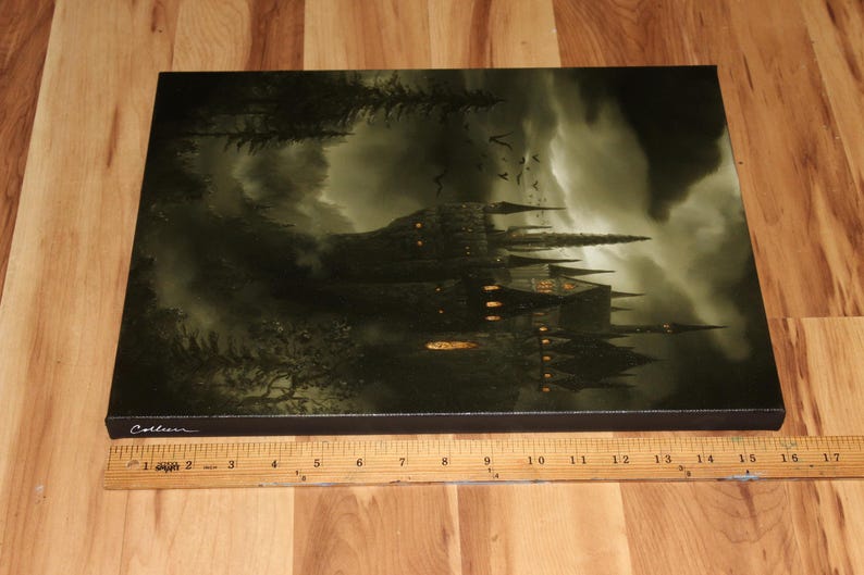 May include: A canvas print depicting a gothic castle under a stormy sky. The artwork features a dark color palette with shades of green and gray, and the castle is illuminated by warm, golden lights. The print is rectangular and rests on a wooden surface.