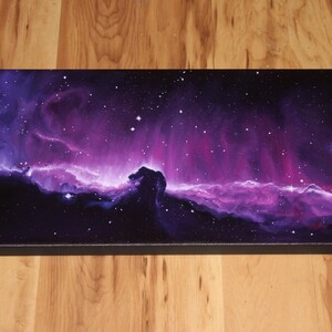 May include: A rectangular canvas print depicting a vibrant nebula in shades of purple, pink, and black. The artwork features a celestial scene with stars and a prominent Horsehead Nebula formation. The canvas is stretched on a black frame.