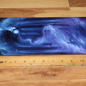 May include: A rectangular canvas painting featuring a dark blue and purple cosmic nebula scene with a glowing white orb and ethereal wisps. A wooden ruler placed along the bottom edge shows the painting is approximately 12 inches in length.